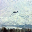 In the distance, an American Apache attack helicopter patrols the huge, white blanketed mountains