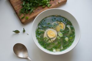 Summer green soup - bouillon with noodles, egg and spring onion - on white background
