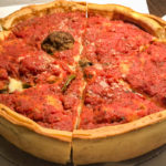 A thick and tall deep dish pizza is topped with red sauce and cheese.