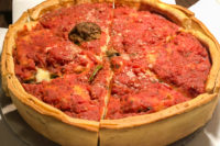 A thick and tall deep dish pizza is topped with red sauce and cheese.