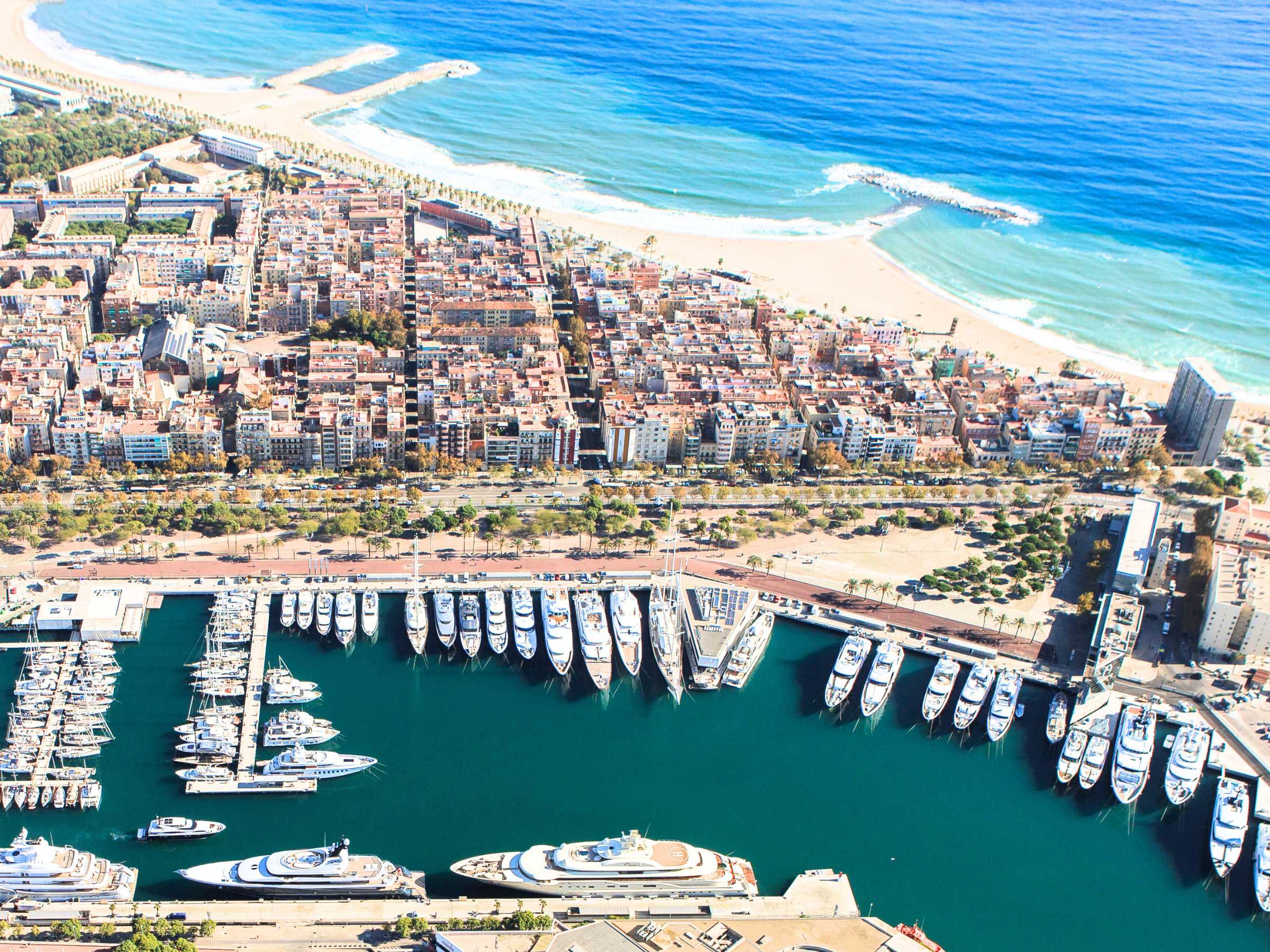 Aerial view of a vibrant coastal city with a bustling marina filled with yachts and boats, set against the backdrop of the Mediterranean Sea's turquoise waters.