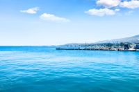 A calm, expansive blue sea with a distant shoreline and mountains under a bright, clear sky, capturing the serene beauty of a Mediterranean coastal landscape.